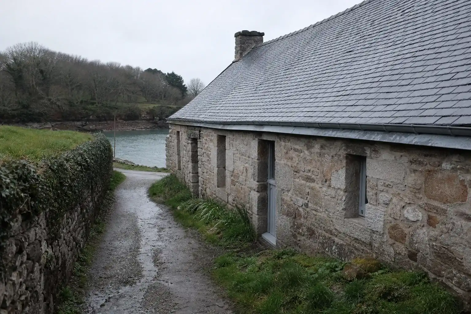 Longère de pierre basse dans le bocage morbihannais, toiture en ardoise et petites ouvertures