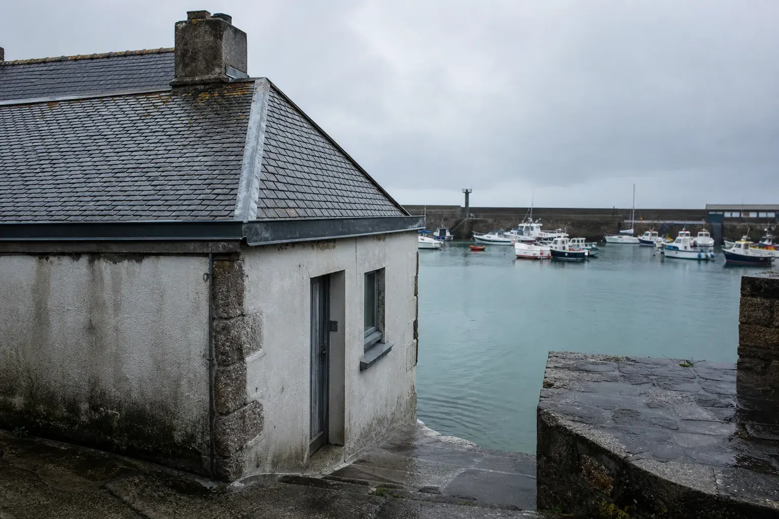 Petite maison de pêcheur face à un bassin portuaire, murs enduits et versant d’ardoise pentu