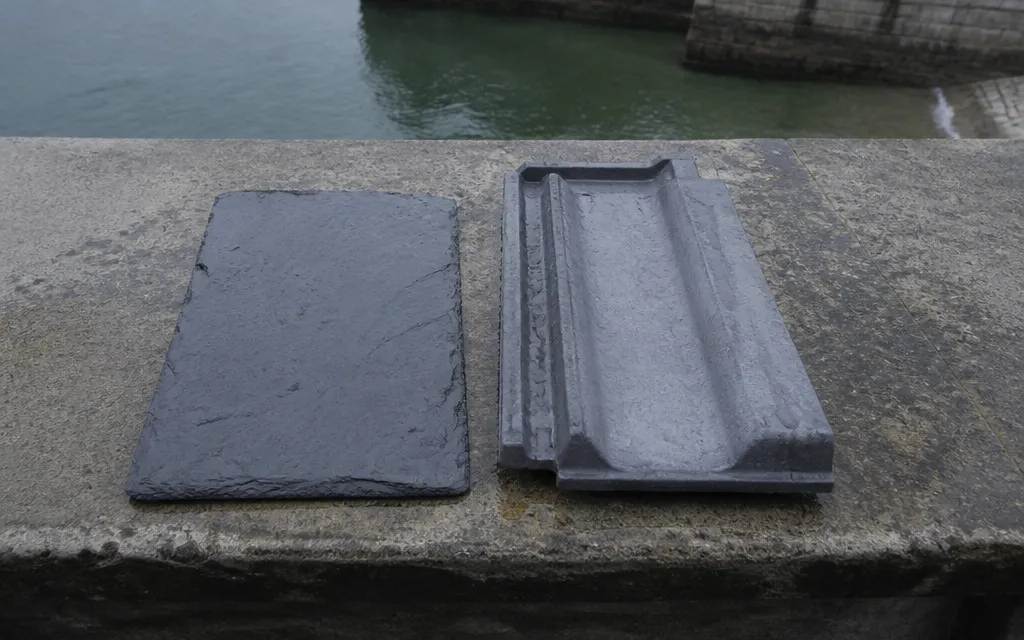 Une ardoise naturelle et une tuile mécanique en terre cuite posées côte à côte sur un établi
