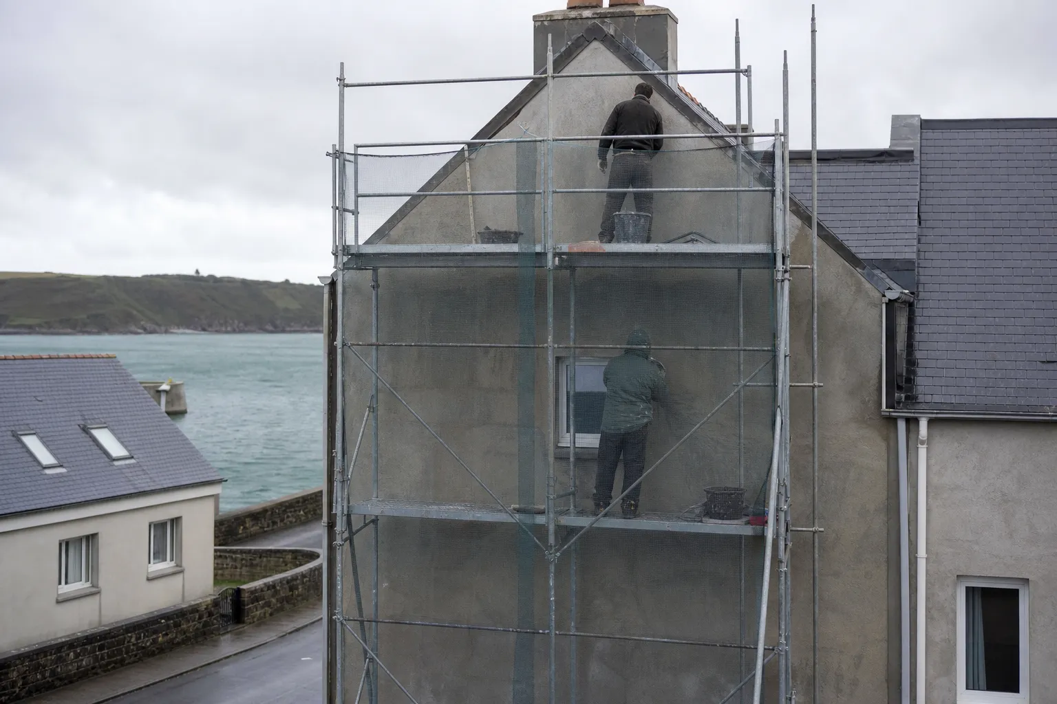 Échafaudage de pied monté contre le pignon d’une maison enduite, filet de sécurité en place